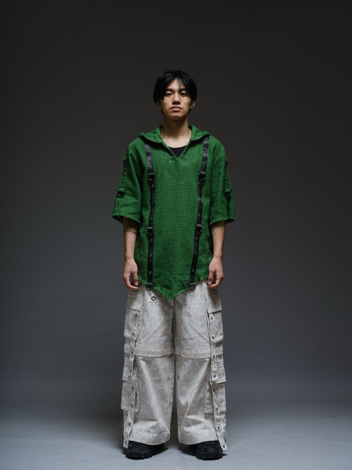 Dark olive hooded poncho with black straps and D-rings, paired with convertible camo denim cargo pants