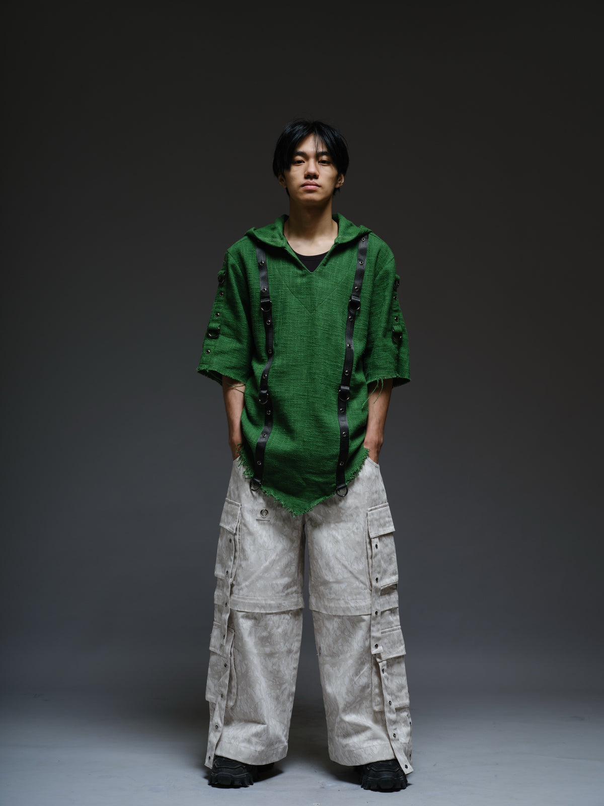 Dark olive hooded poncho with black straps and D-rings, paired with convertible camo denim cargo pants