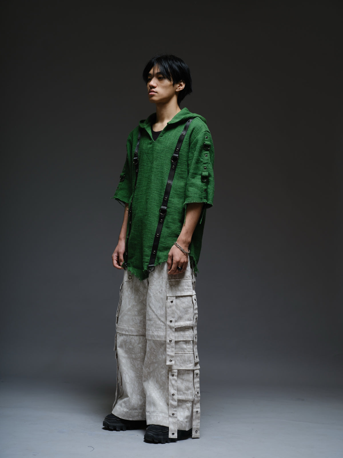 Dark olive hooded poncho with black straps and D-rings, paired with convertible camo denim cargo pants