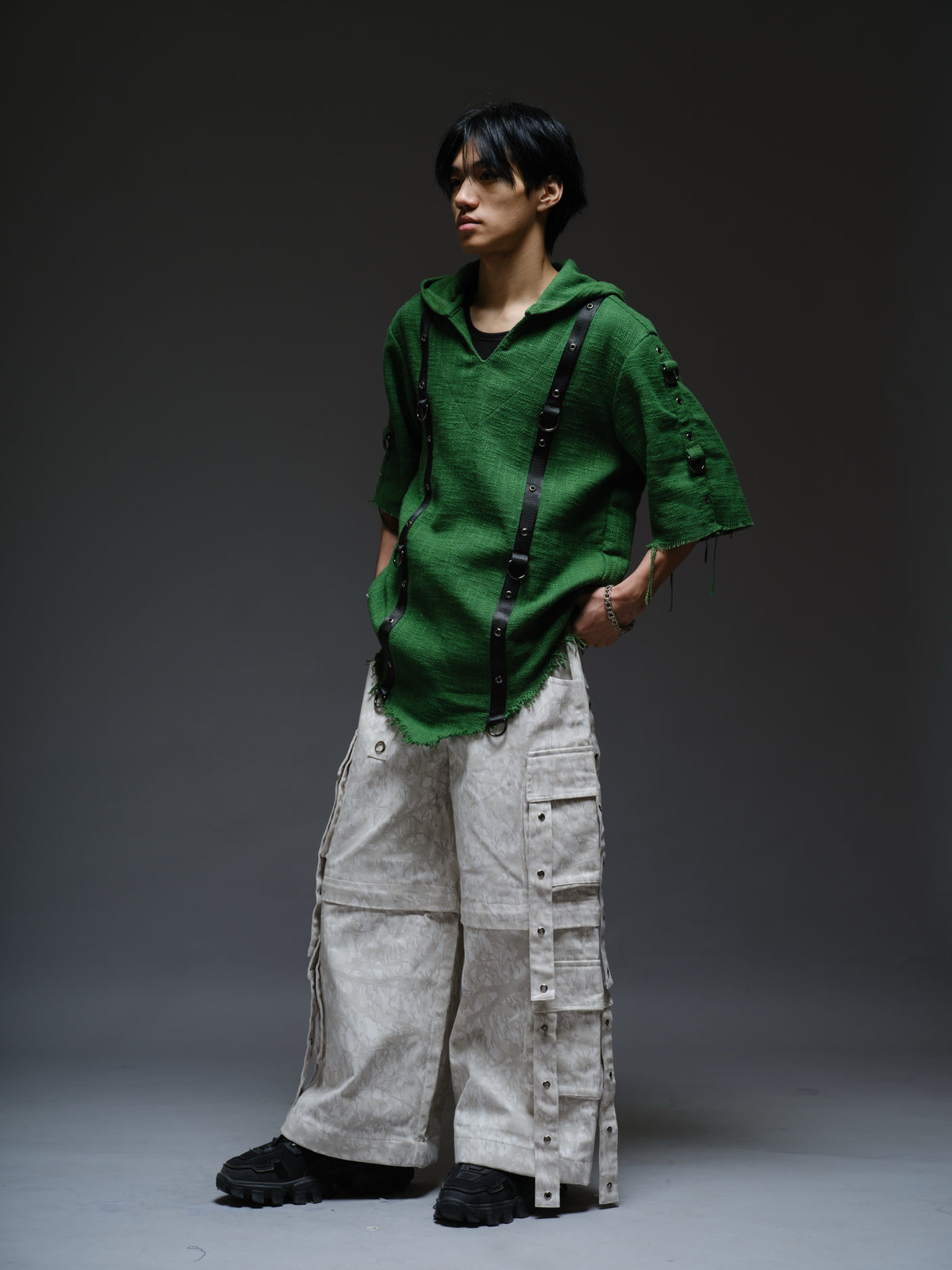 Dark olive hooded poncho with black straps and D-rings, paired with convertible camo denim cargo pants