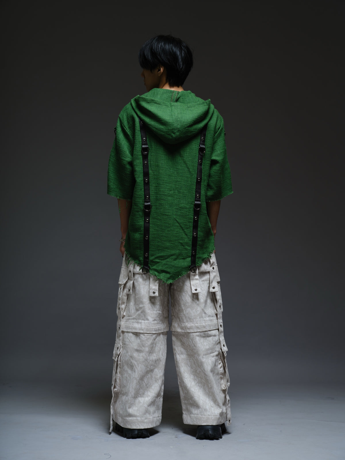 Dark olive hooded poncho with black straps and D-rings, paired with convertible camo denim cargo pants