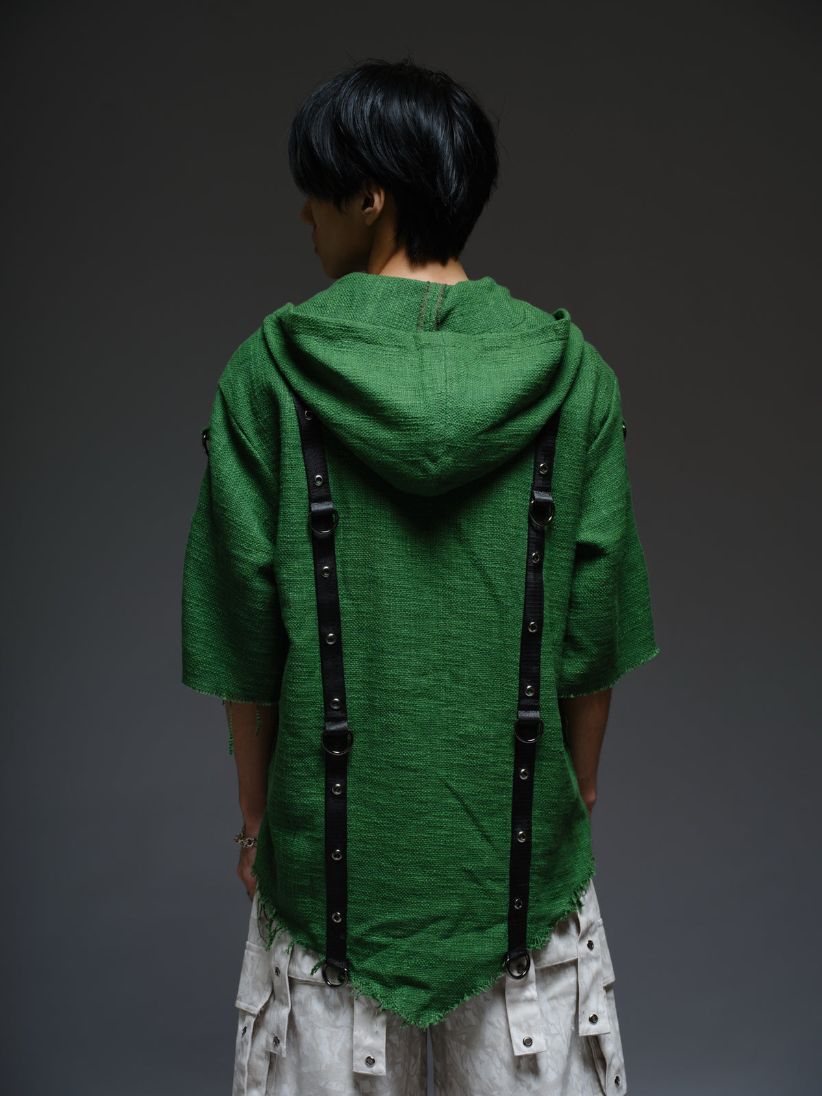 Dark olive hooded poncho with black straps and D-rings, paired with convertible camo denim cargo pants