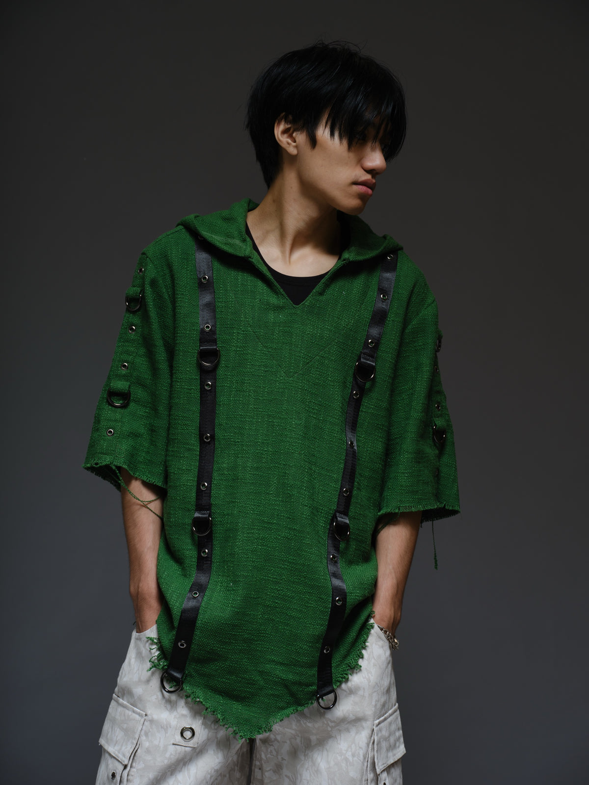 Dark olive hooded poncho with black straps and D-rings, paired with convertible camo denim cargo pants