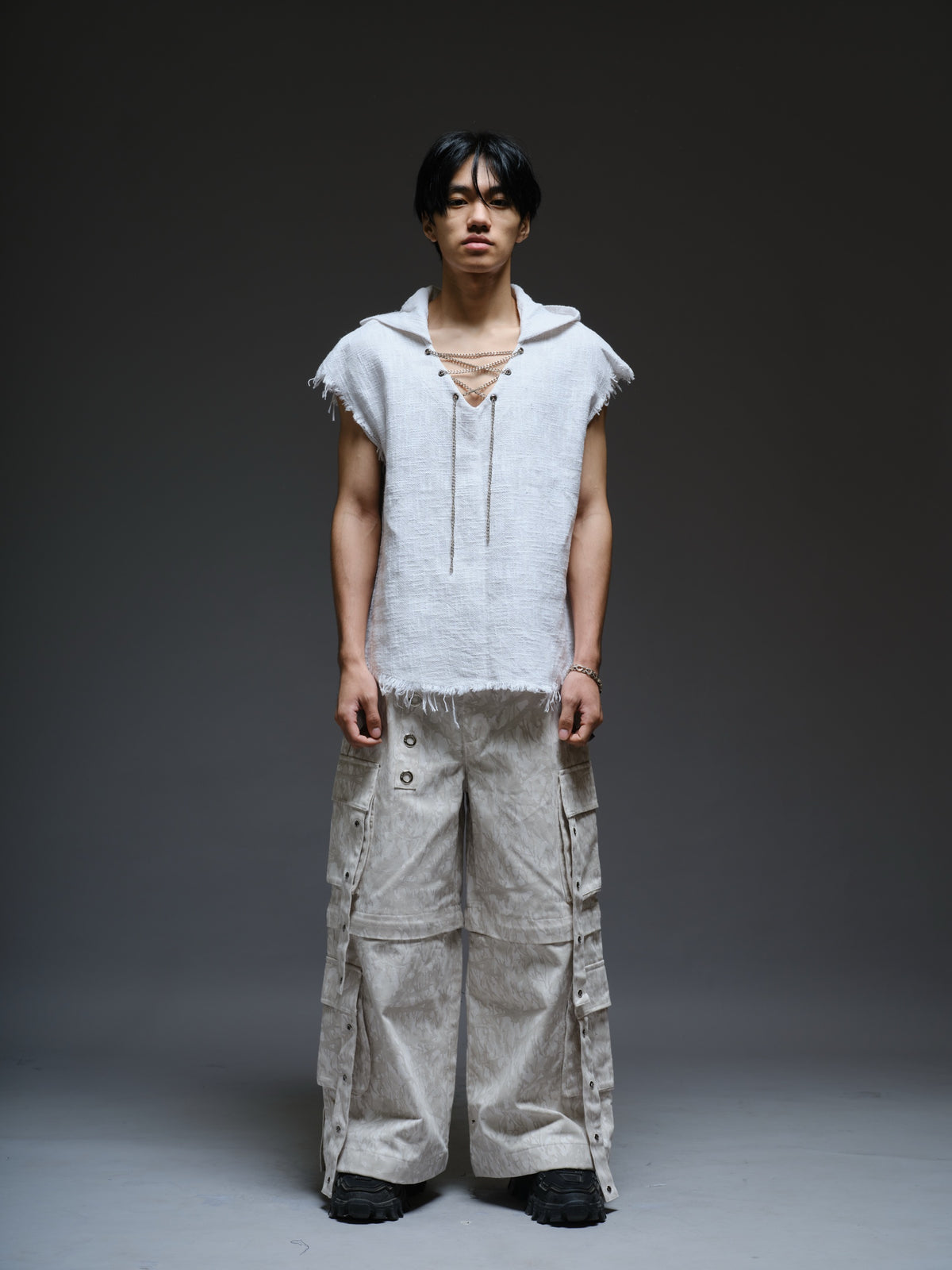 Sleeveless hooded cotton jute top with frayed edges, paired with printed camo denim cargo pants with oversized flap pockets and hanging straps