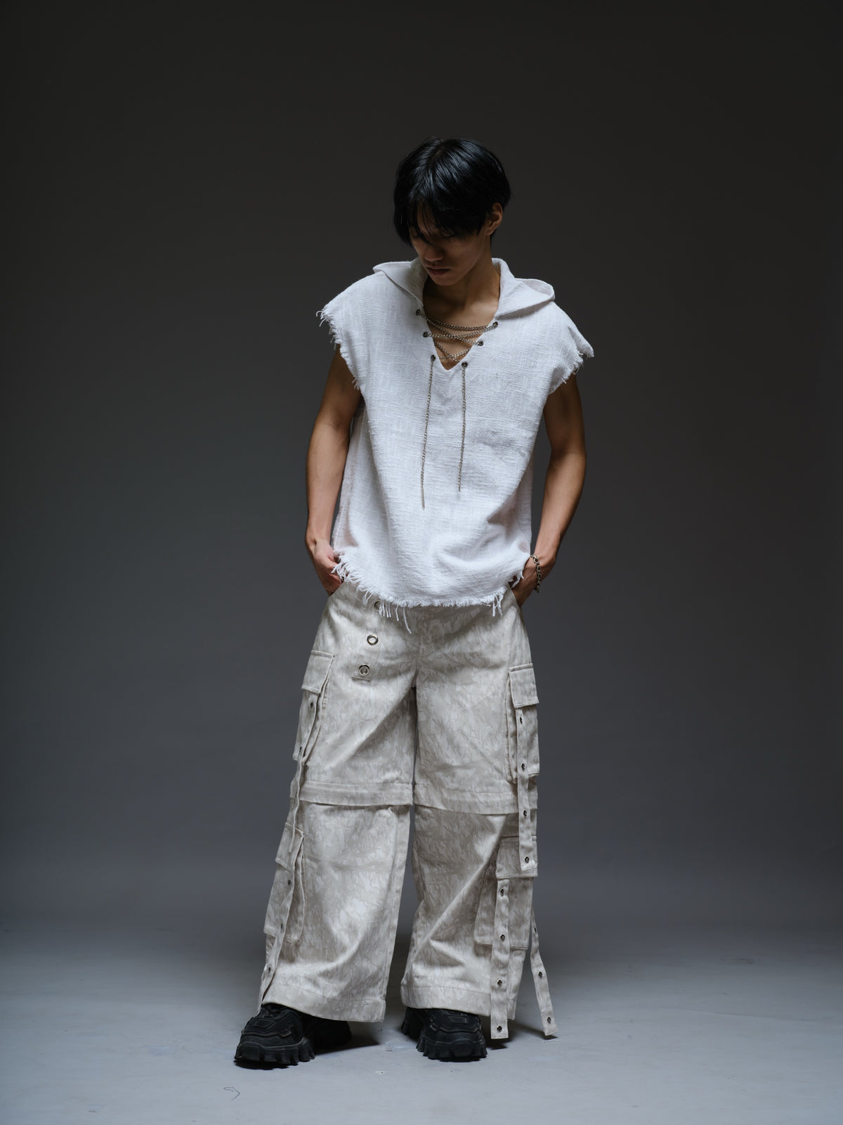 Sleeveless hooded cotton jute top with frayed edges, paired with printed camo denim cargo pants with oversized flap pockets and hanging straps