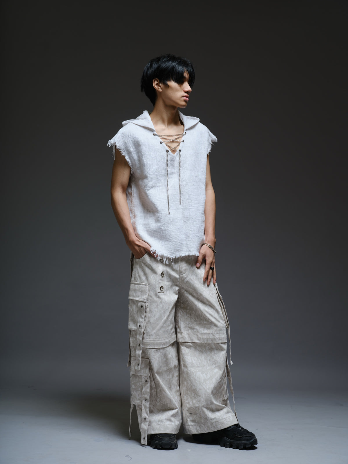 Sleeveless hooded cotton jute top with frayed edges, paired with printed camo denim cargo pants with oversized flap pockets and hanging straps