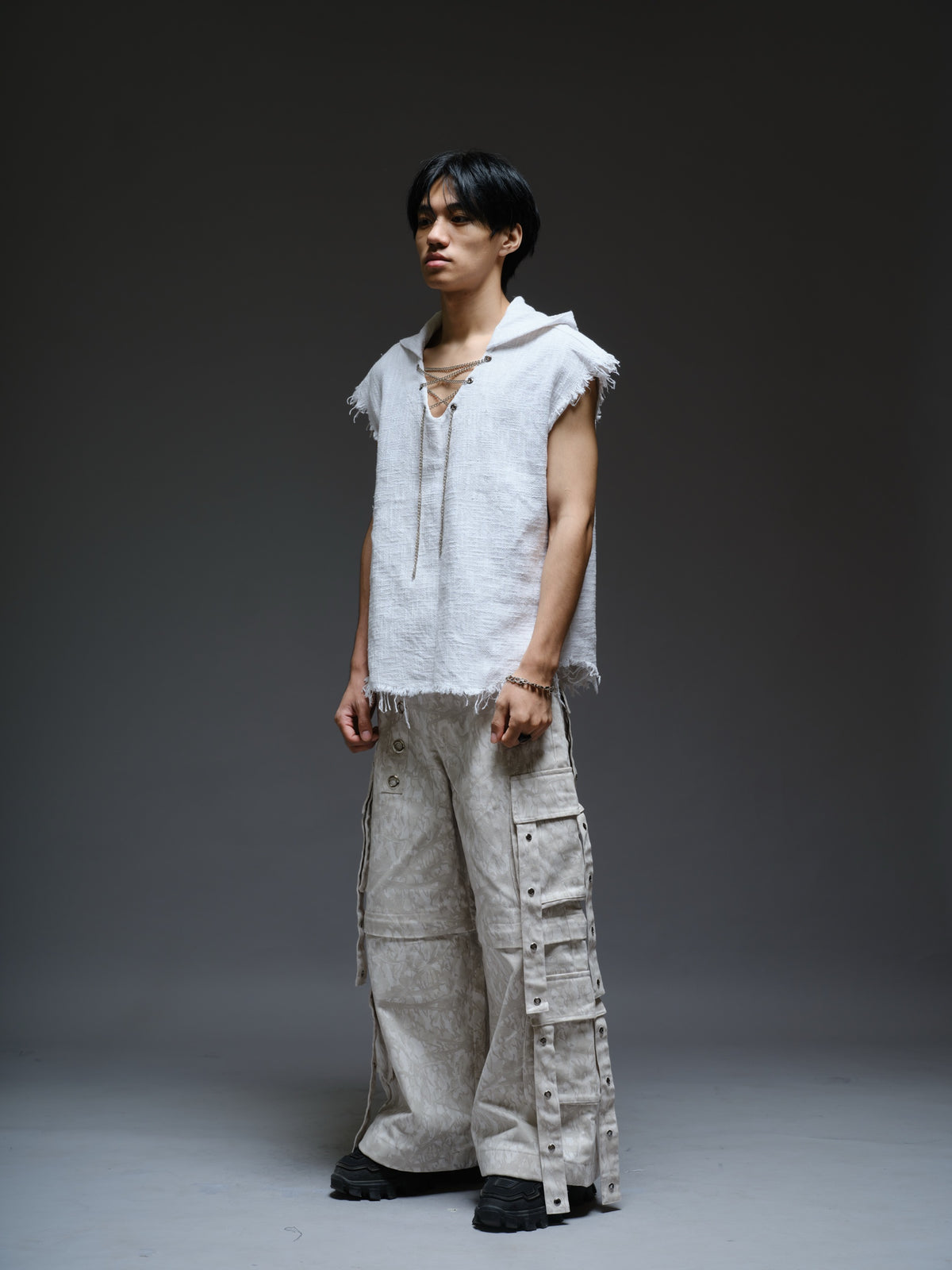 Sleeveless hooded cotton jute top with frayed edges, paired with printed camo denim cargo pants with oversized flap pockets and hanging straps