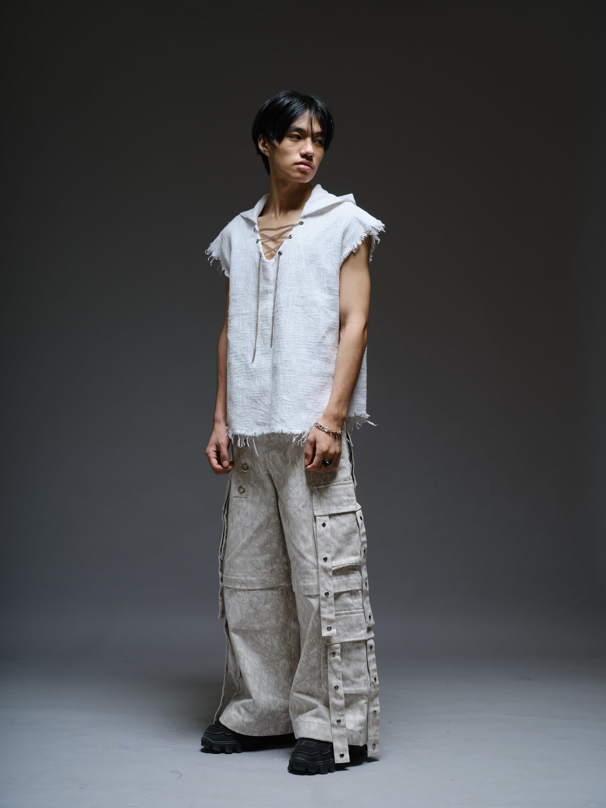 Sleeveless hooded cotton jute top with frayed edges, paired with printed camo denim cargo pants with oversized flap pockets and hanging straps