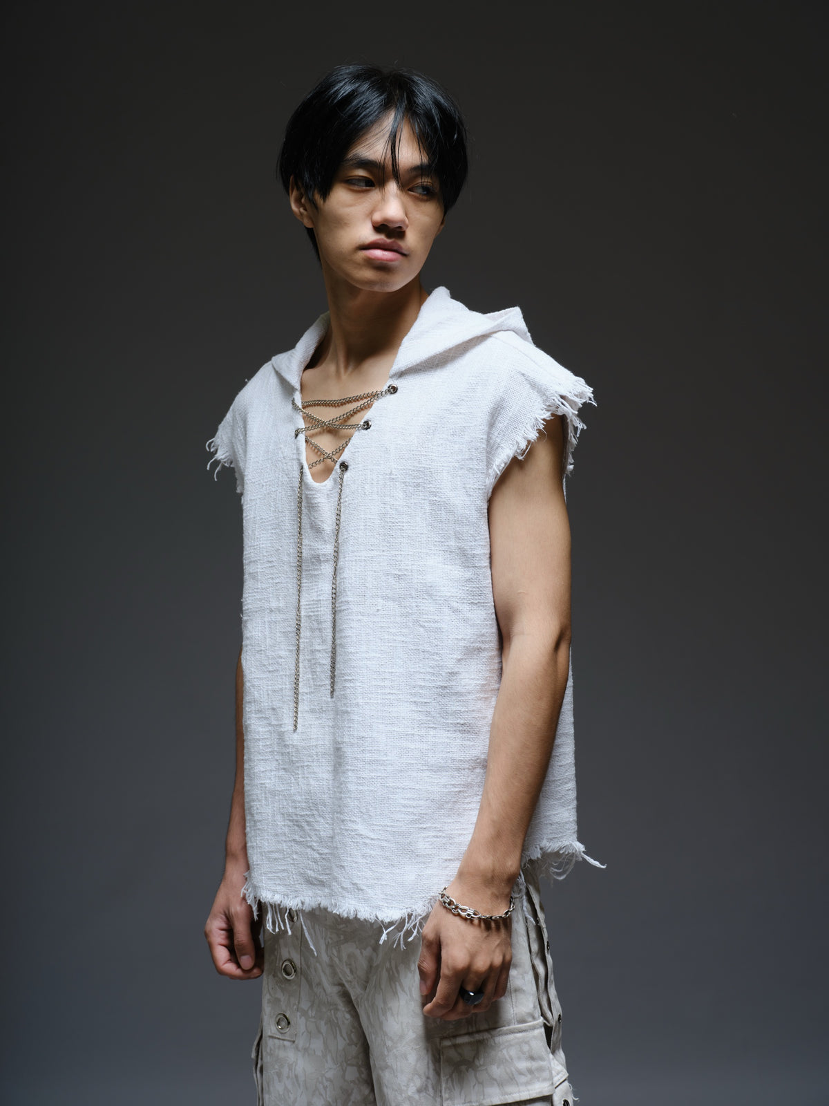 Sleeveless hooded cotton jute top with frayed edges, paired with printed camo denim cargo pants with oversized flap pockets and hanging straps