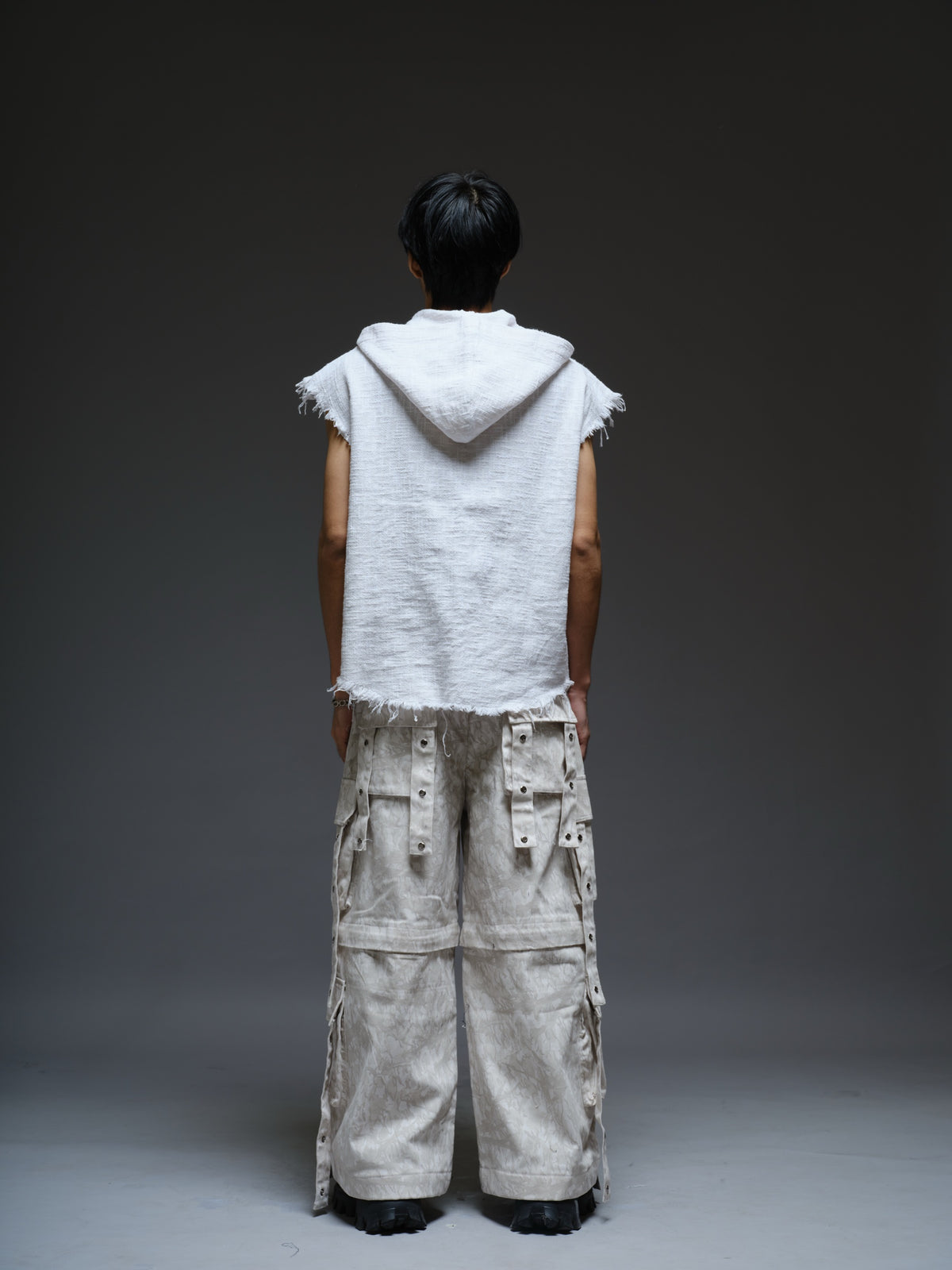 Sleeveless hooded cotton jute top with frayed edges, paired with printed camo denim cargo pants with oversized flap pockets and hanging straps