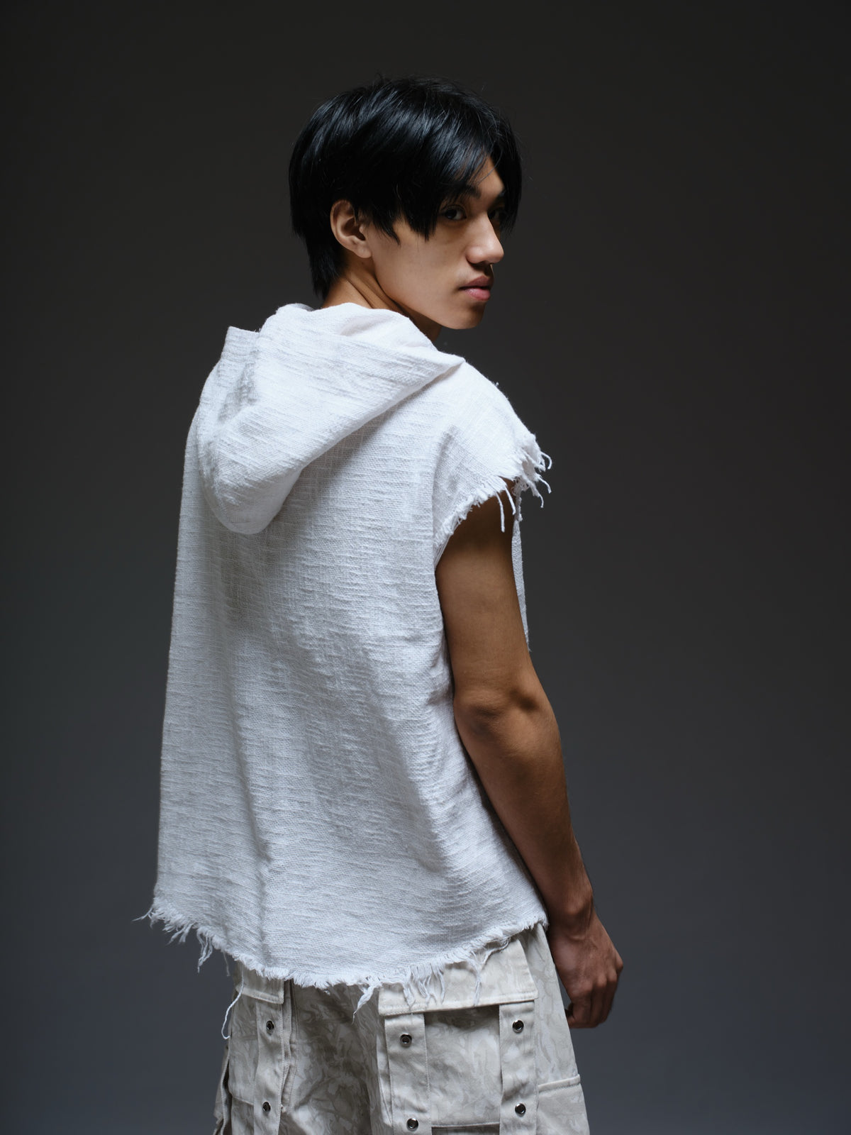 Sleeveless hooded cotton jute top with frayed edges, paired with printed camo denim cargo pants with oversized flap pockets and hanging straps