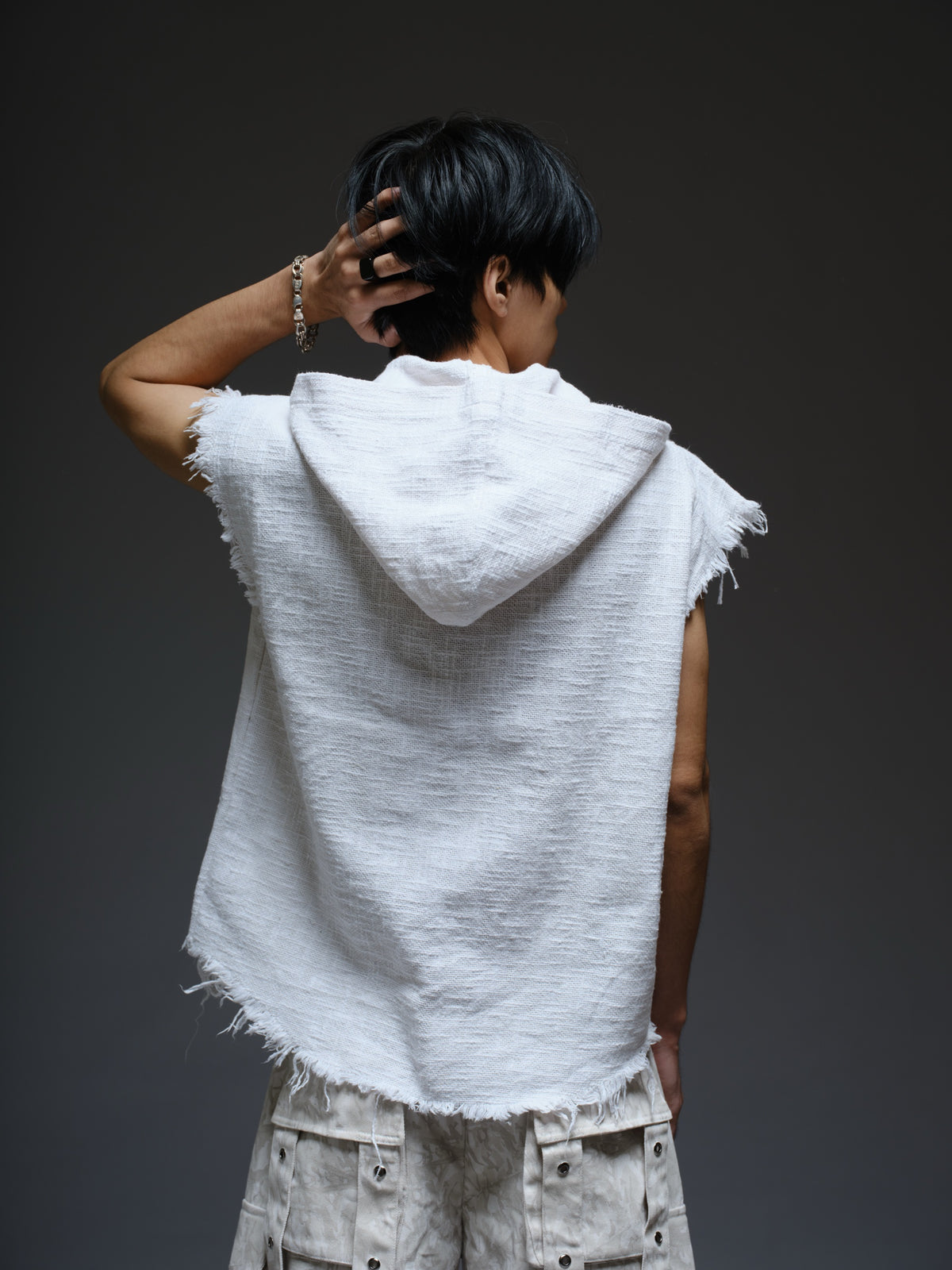 Sleeveless hooded cotton jute top with frayed edges, paired with printed camo denim cargo pants with oversized flap pockets and hanging straps