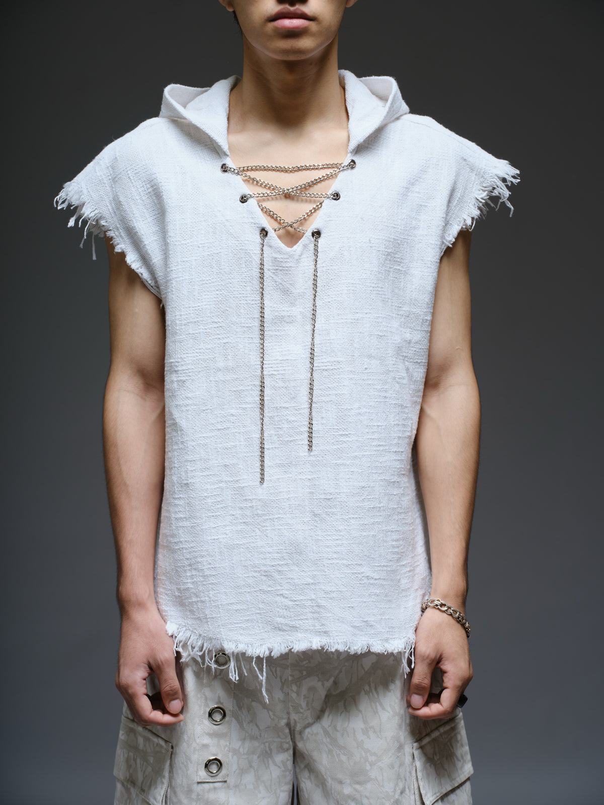 Sleeveless hooded cotton jute top with frayed edges, paired with printed camo denim cargo pants with oversized flap pockets and hanging straps
