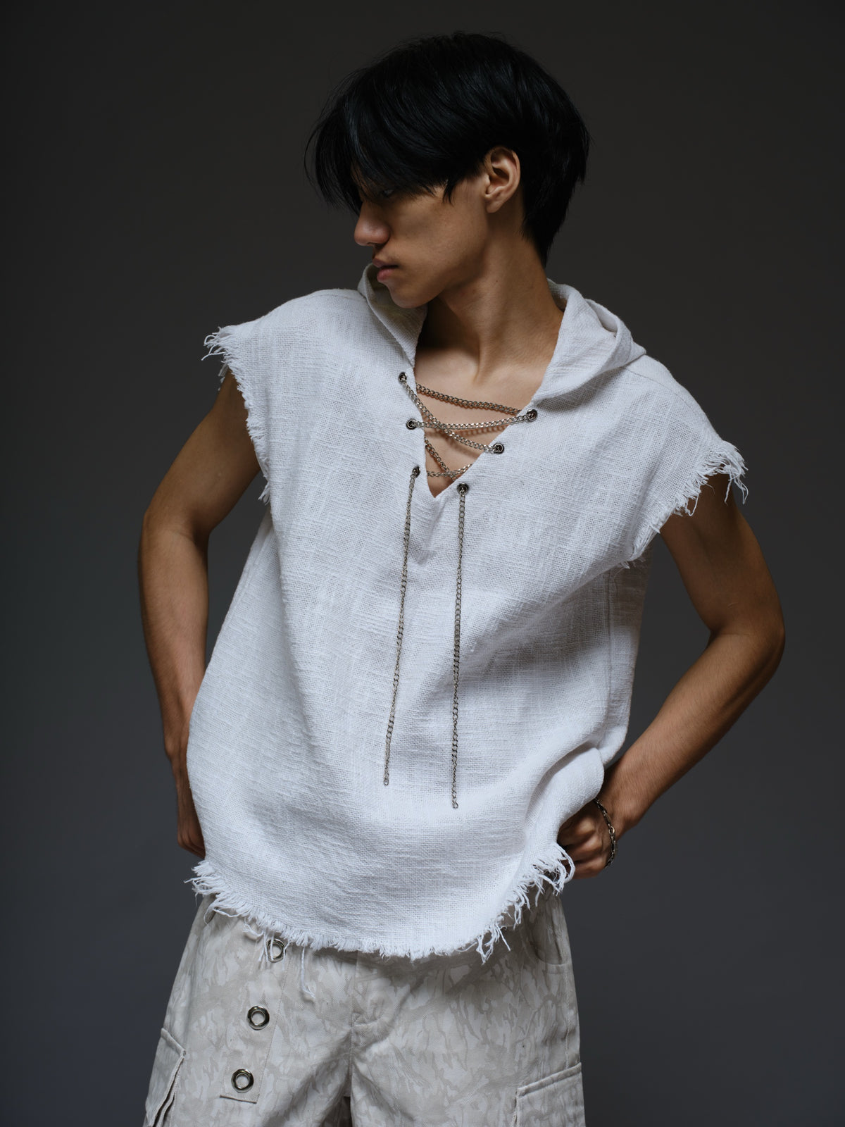 Sleeveless hooded cotton jute top with frayed edges, paired with printed camo denim cargo pants with oversized flap pockets and hanging straps