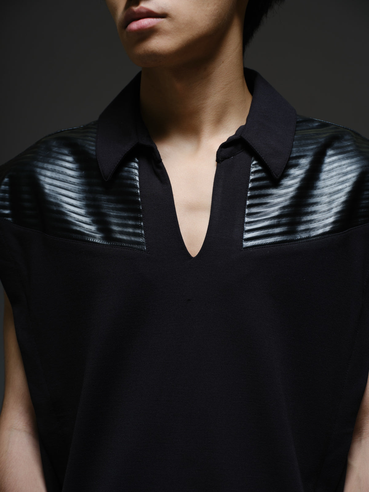 Onyx black sleeveless Roma knit tee with extended shoulders, stitched leather chest panels, a pointed collar and an open V neckline