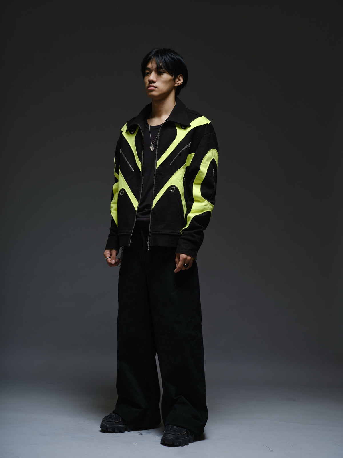 Black denim jacket with neon panels across the chest and sleeves, decorative silver zippers, large metal eyelets and a broad collar.