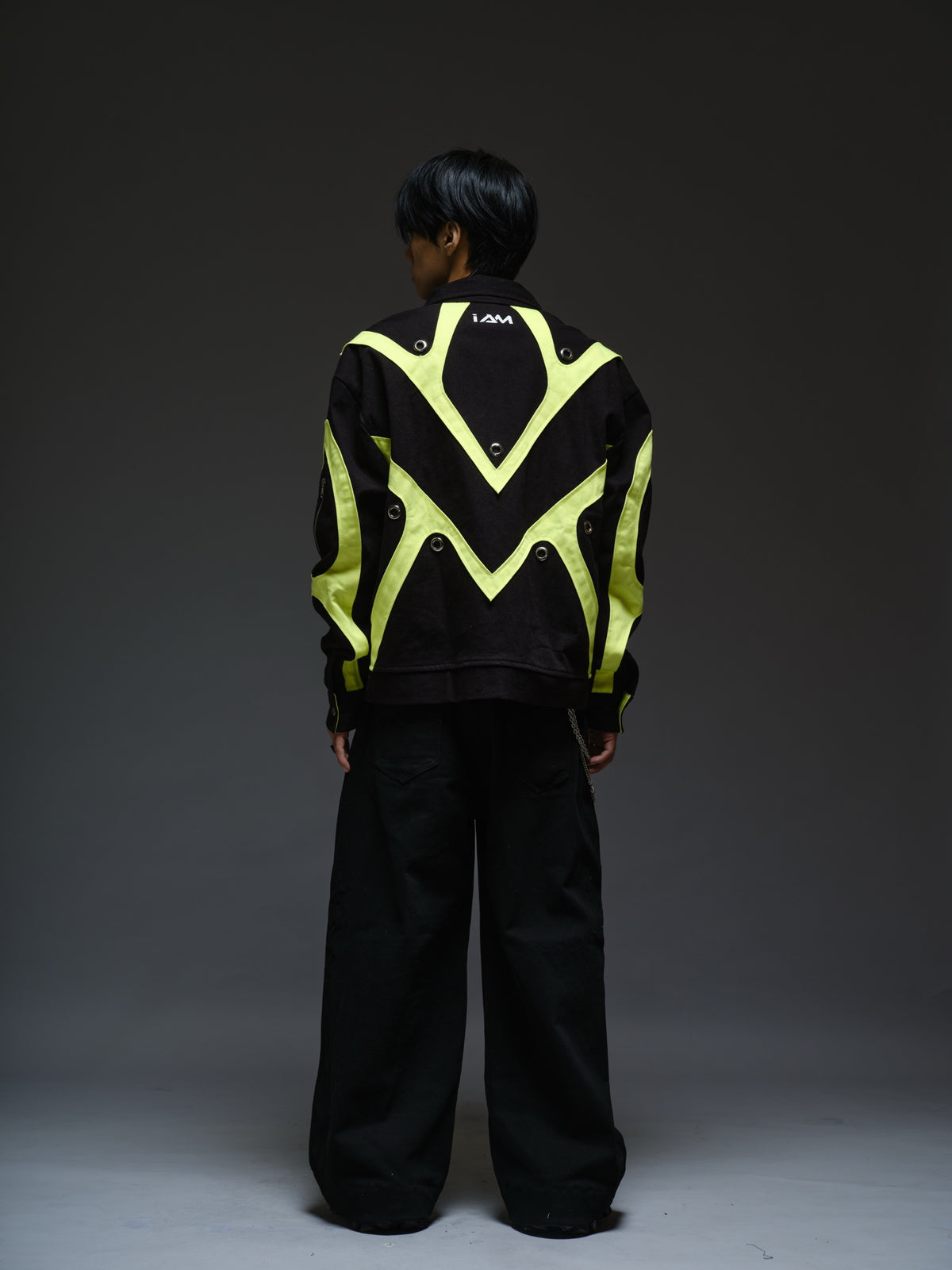 Black denim jacket with neon panels across the chest and sleeves, decorative silver zippers, large metal eyelets and a broad collar.