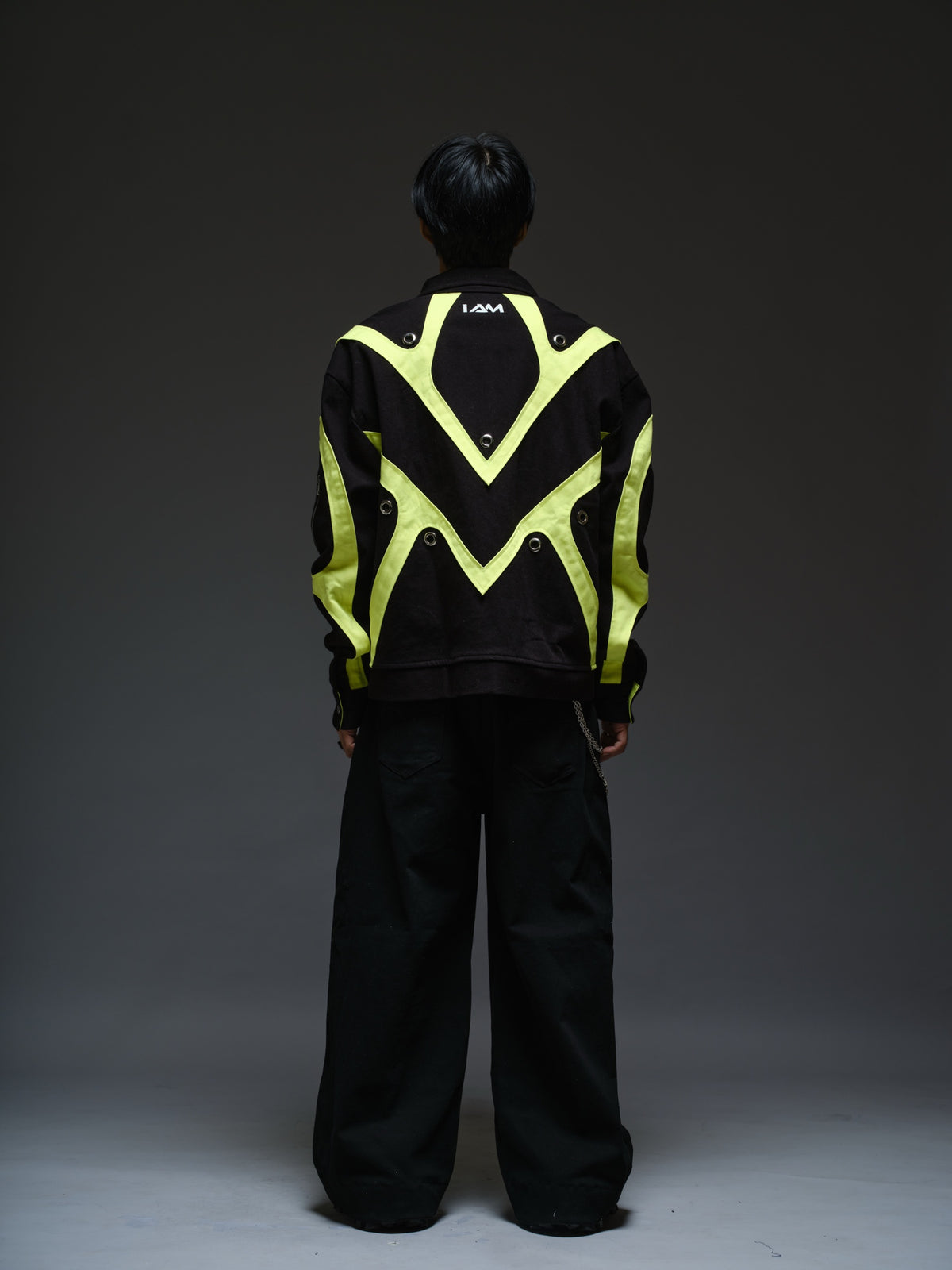 Black denim jacket with neon panels across the chest and sleeves, decorative silver zippers, large metal eyelets and a broad collar.