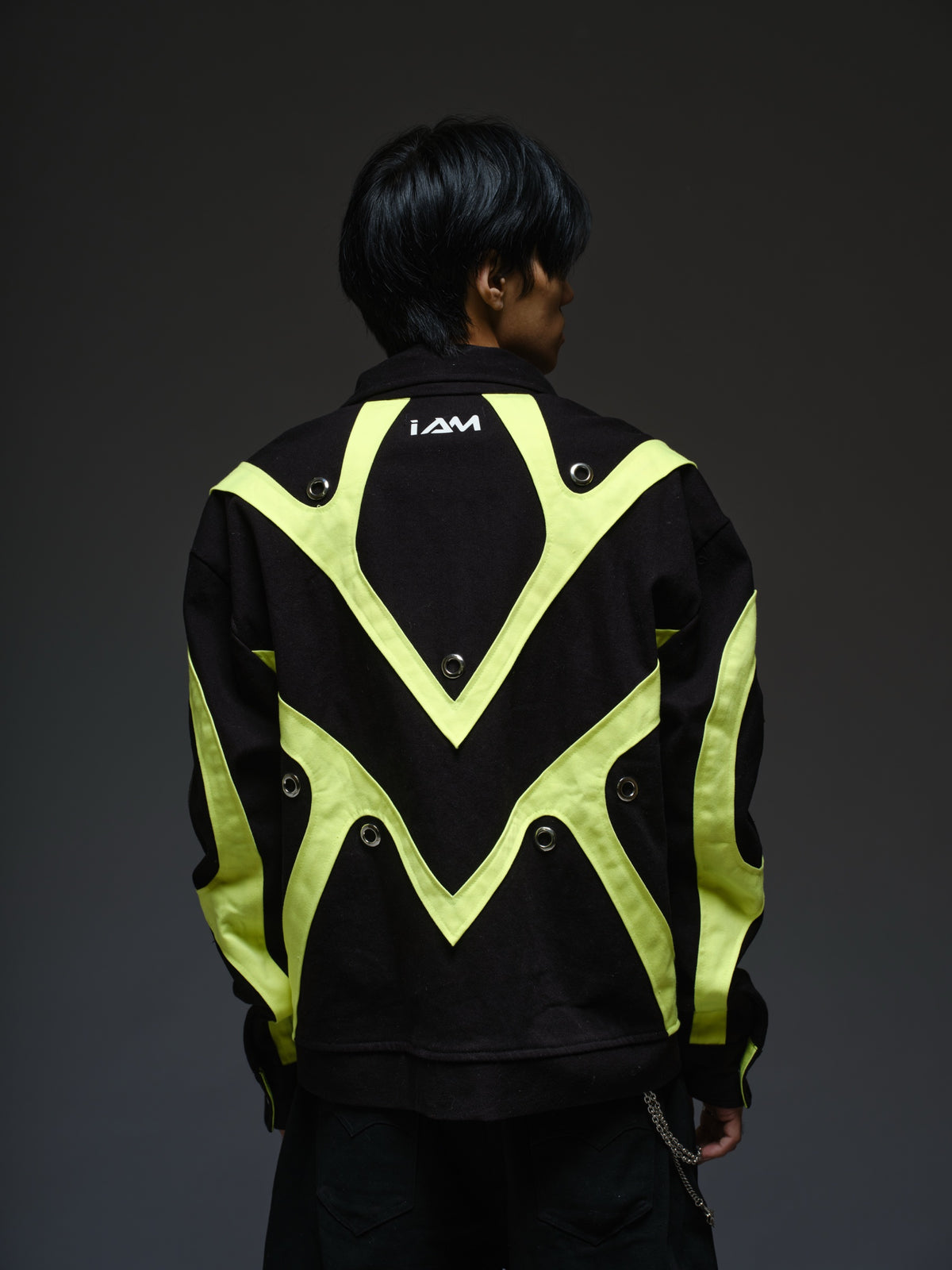 Black denim jacket with neon panels across the chest and sleeves, decorative silver zippers, large metal eyelets and a broad collar.