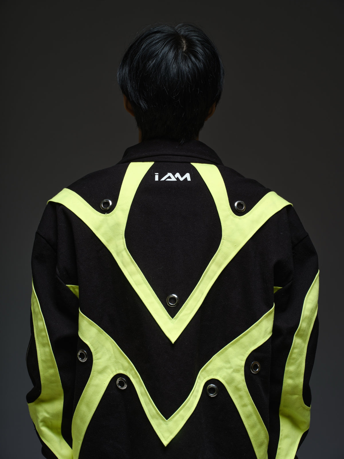 Black denim jacket with neon panels across the chest and sleeves, decorative silver zippers, large metal eyelets and a broad collar.
