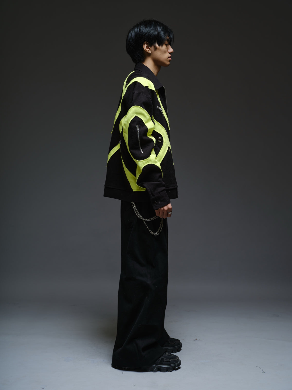 Black denim jacket with neon panels across the chest and sleeves, decorative silver zippers, large metal eyelets and a broad collar.