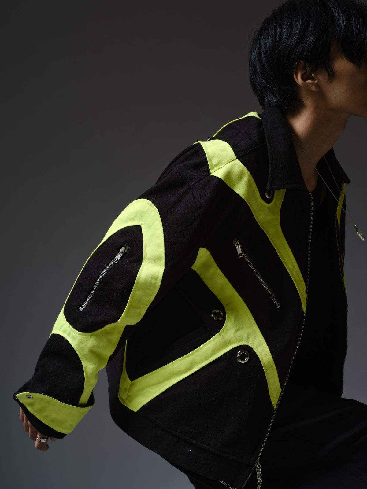 Black denim jacket with neon panels across the chest and sleeves, decorative silver zippers, large metal eyelets and a broad collar.