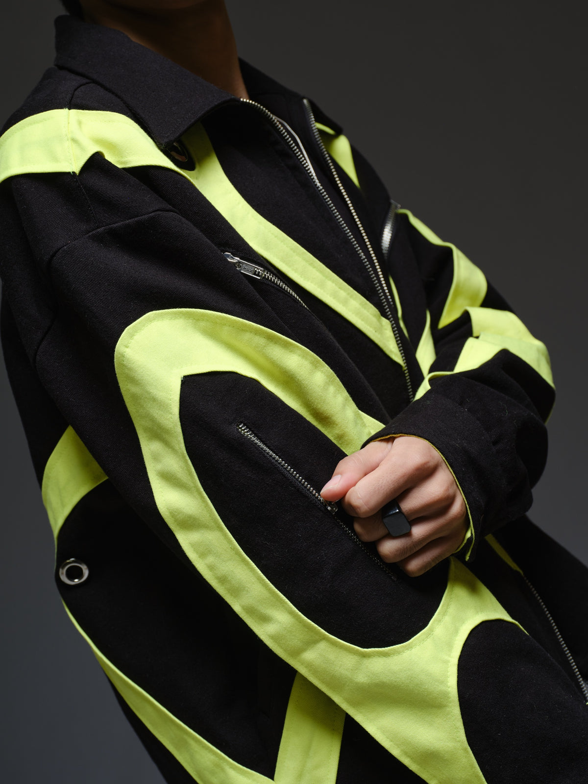 Black denim jacket with neon panels across the chest and sleeves, decorative silver zippers, large metal eyelets and a broad collar.