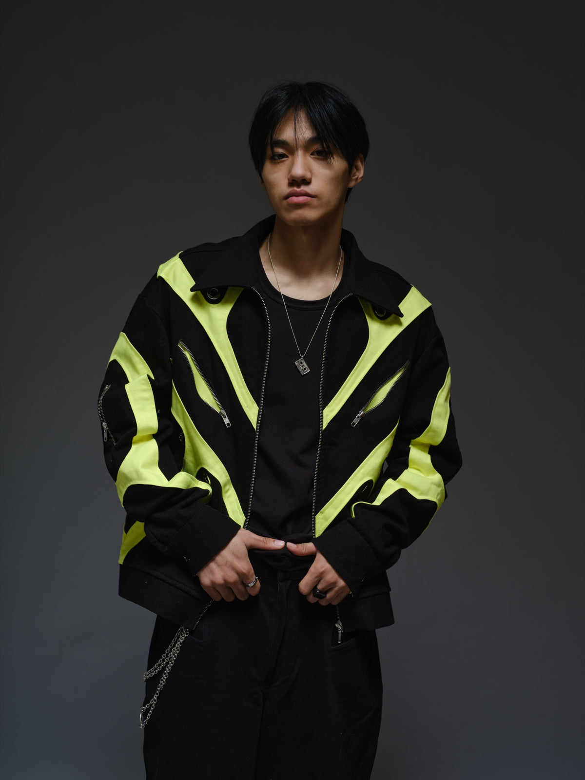 Black denim jacket with neon panels across the chest and sleeves, decorative silver zippers, large metal eyelets and a broad collar.