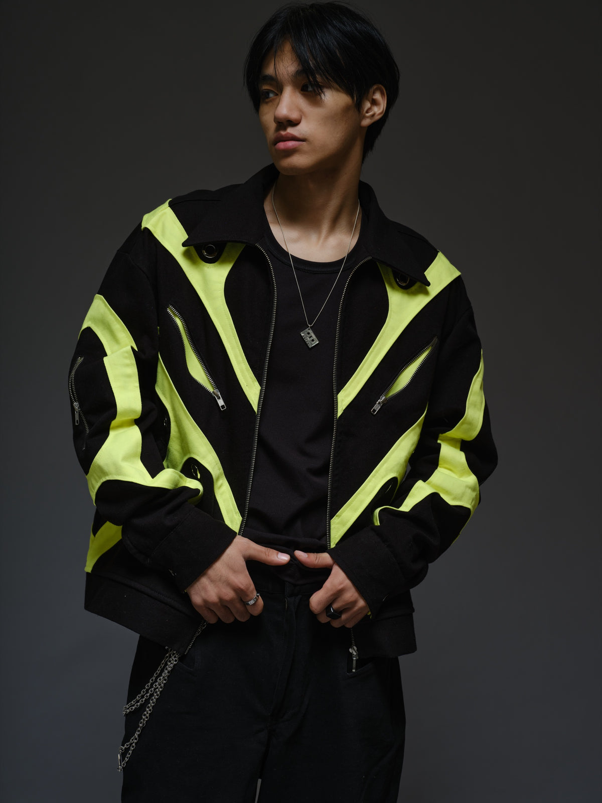 Black denim jacket with neon panels across the chest and sleeves, decorative silver zippers, large metal eyelets and a broad collar.