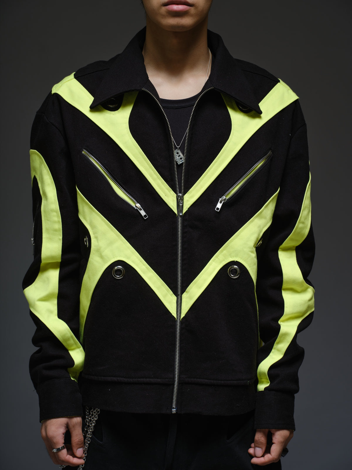 Black denim jacket with neon panels across the chest and sleeves, decorative silver zippers, large metal eyelets and a broad collar.