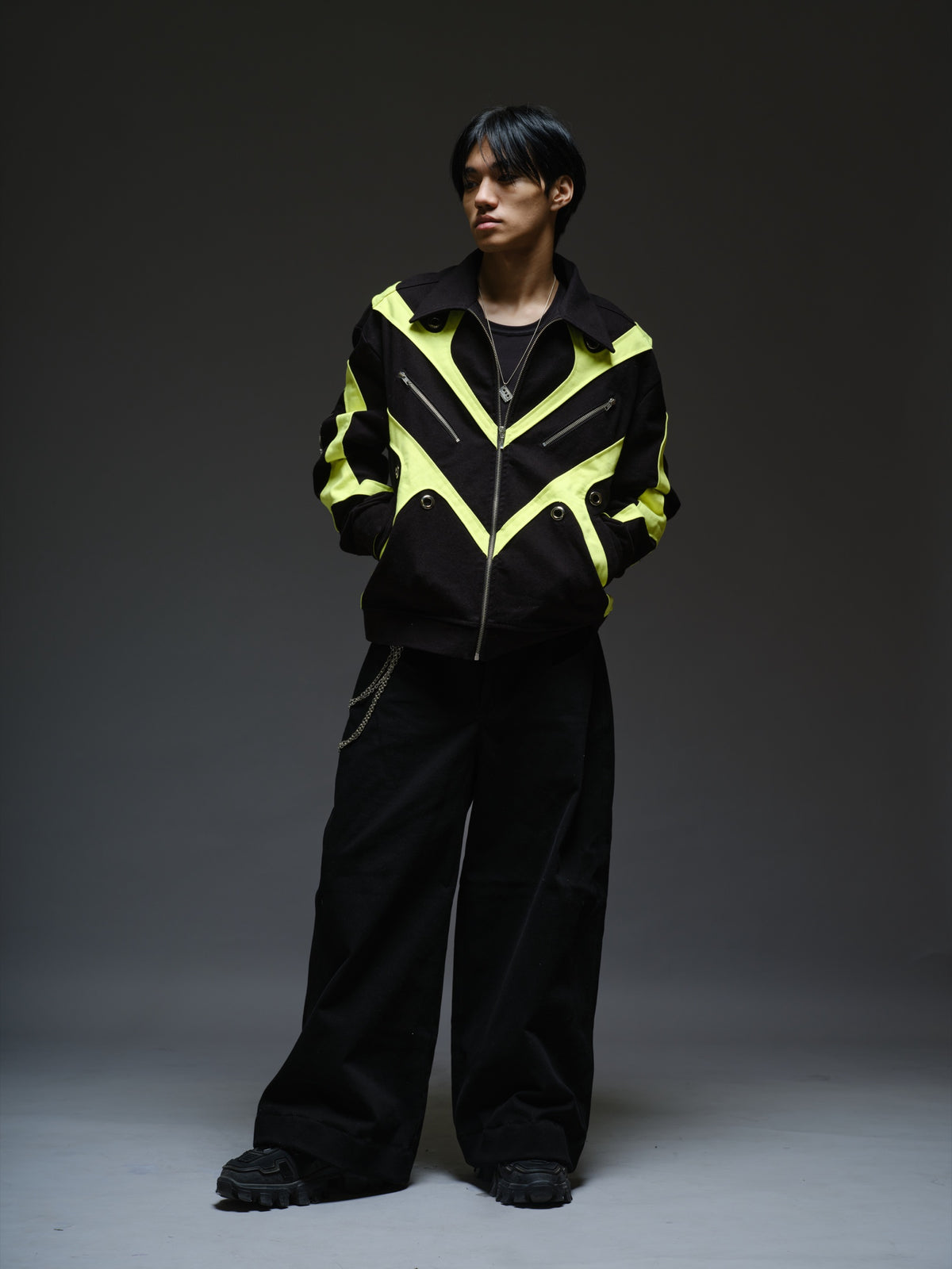 Black denim jacket with neon panels across the chest and sleeves, decorative silver zippers, large metal eyelets and a broad collar.