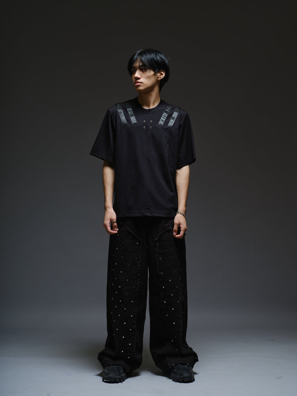 Relaxed black Roma knit T-shirt with angled black leather shoulder straps, four centre-chest rivets and short sleeves.