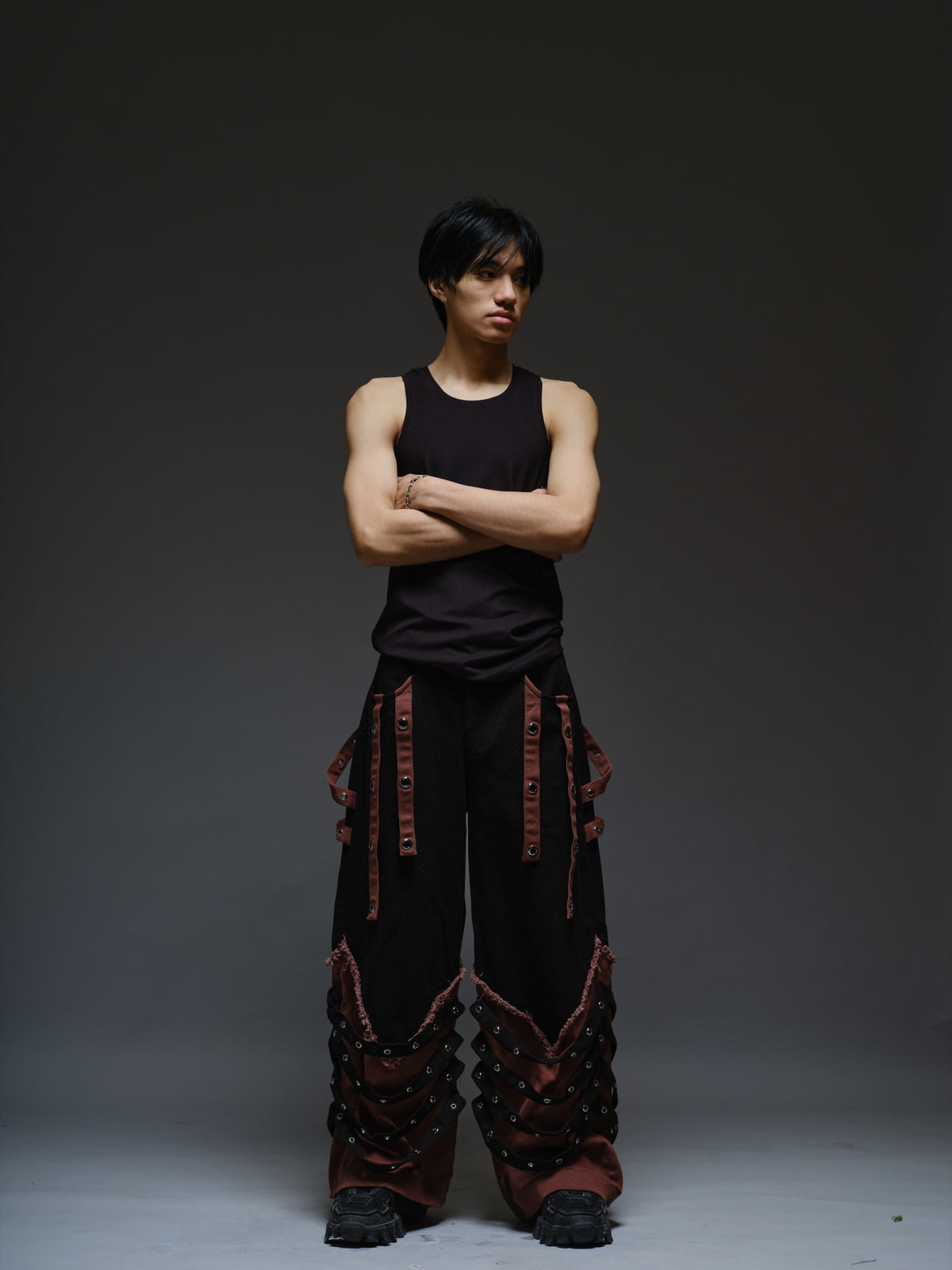 Black wide-leg baggy denim pants with brown hanging straps, layered lower-leg panels, metallic rivets and frayed brown trim