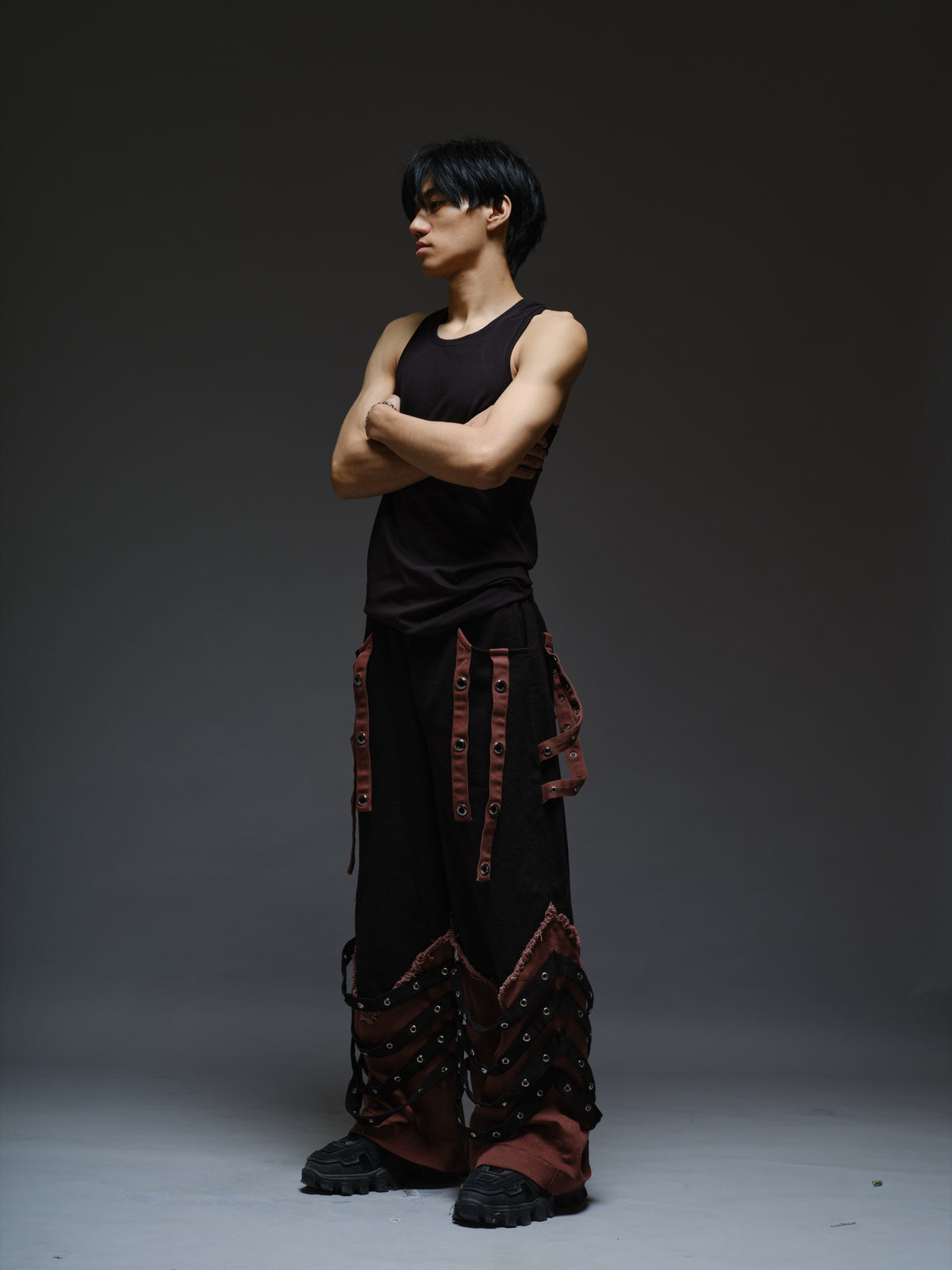 Black wide-leg baggy denim pants with brown hanging straps, layered lower-leg panels, metallic rivets and frayed brown trim