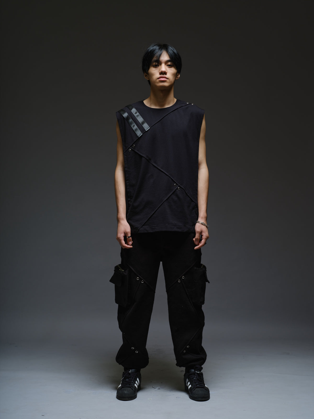 Black sleeveless tee with diagonal panels and leather shoulder patches, paired with black denim track pants with thigh pouch pockets and gathered ankle hems