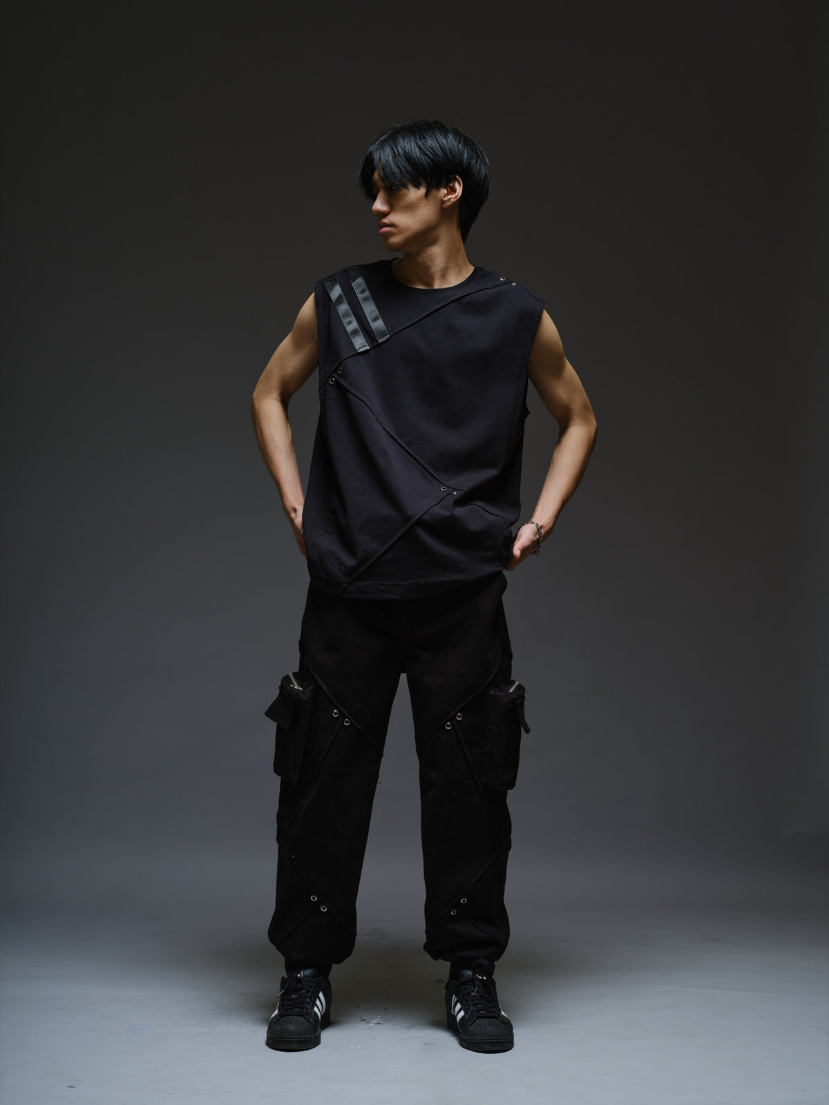 Black sleeveless tee with diagonal panels and leather shoulder patches, paired with black denim track pants with thigh pouch pockets and gathered ankle hems
