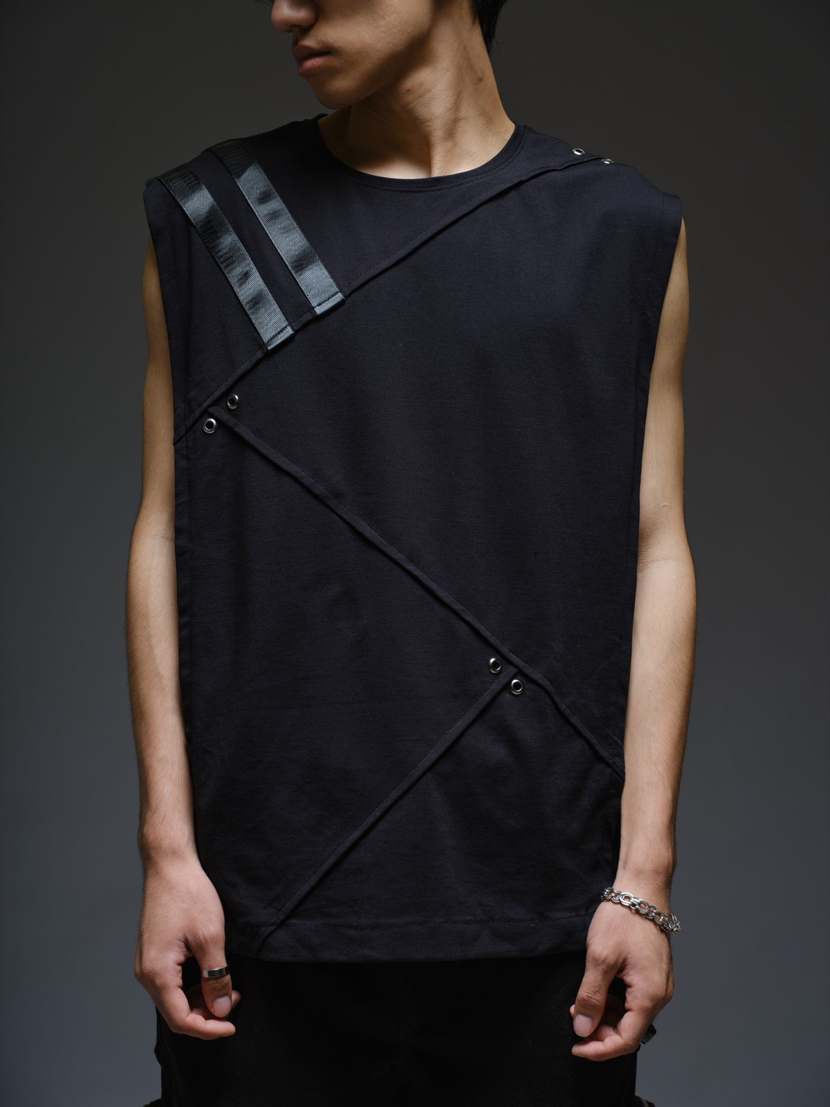 Black sleeveless tee with diagonal panels and leather shoulder patches, paired with black denim track pants with thigh pouch pockets and gathered ankle hems