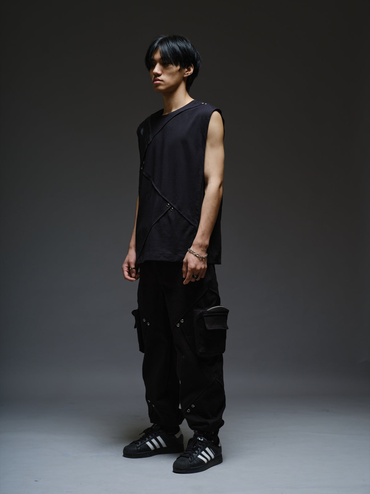 Black sleeveless tee with diagonal panels and leather shoulder patches, paired with black denim track pants with thigh pouch pockets and gathered ankle hems