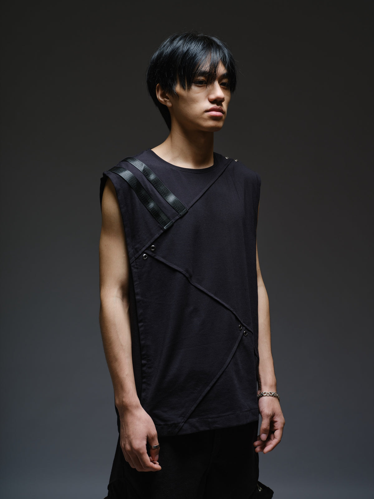 Black sleeveless tee with diagonal panels and leather shoulder patches, paired with black denim track pants with thigh pouch pockets and gathered ankle hems