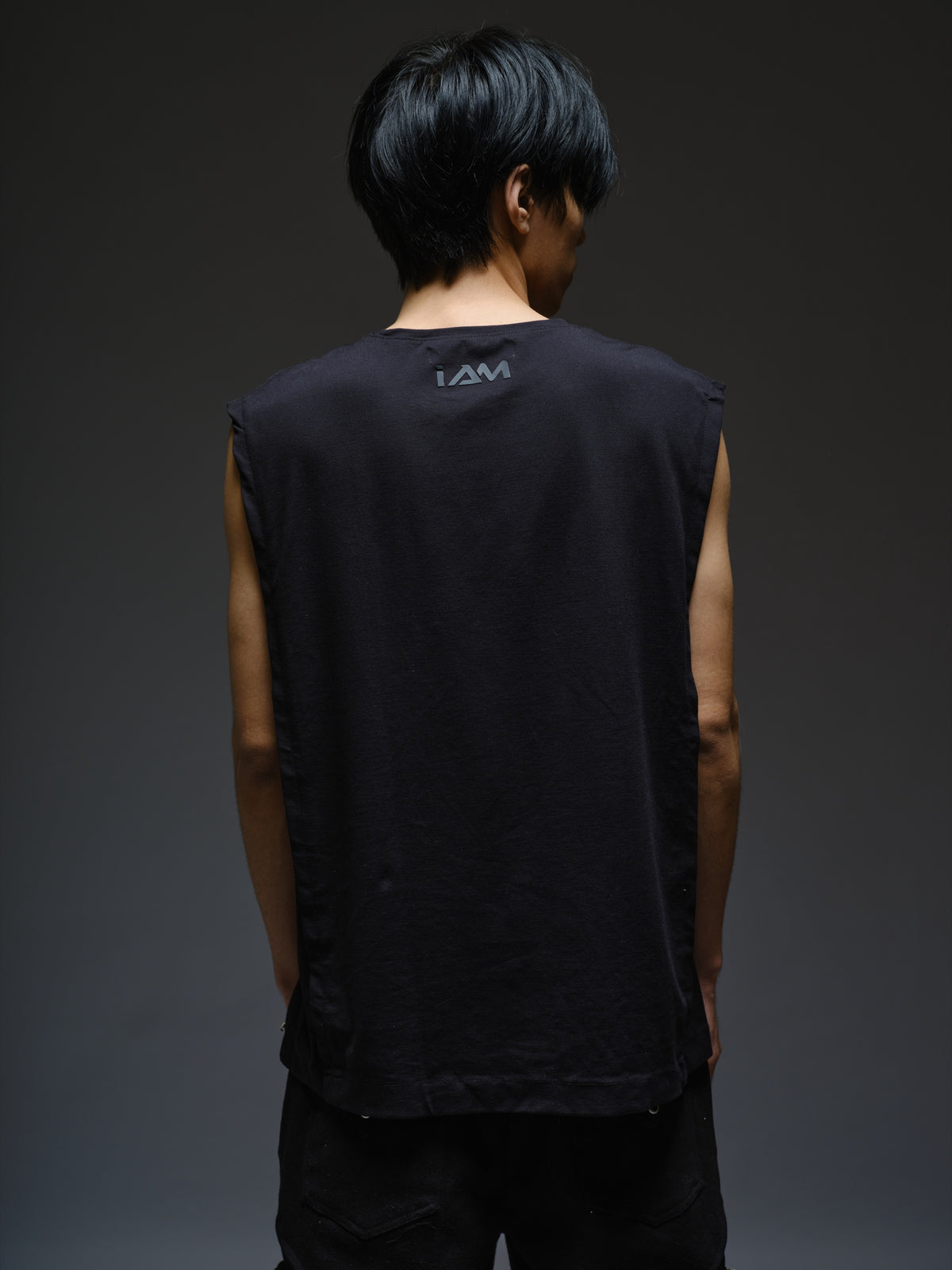 Black sleeveless tee with diagonal panels and leather shoulder patches, paired with black denim track pants with thigh pouch pockets and gathered ankle hems