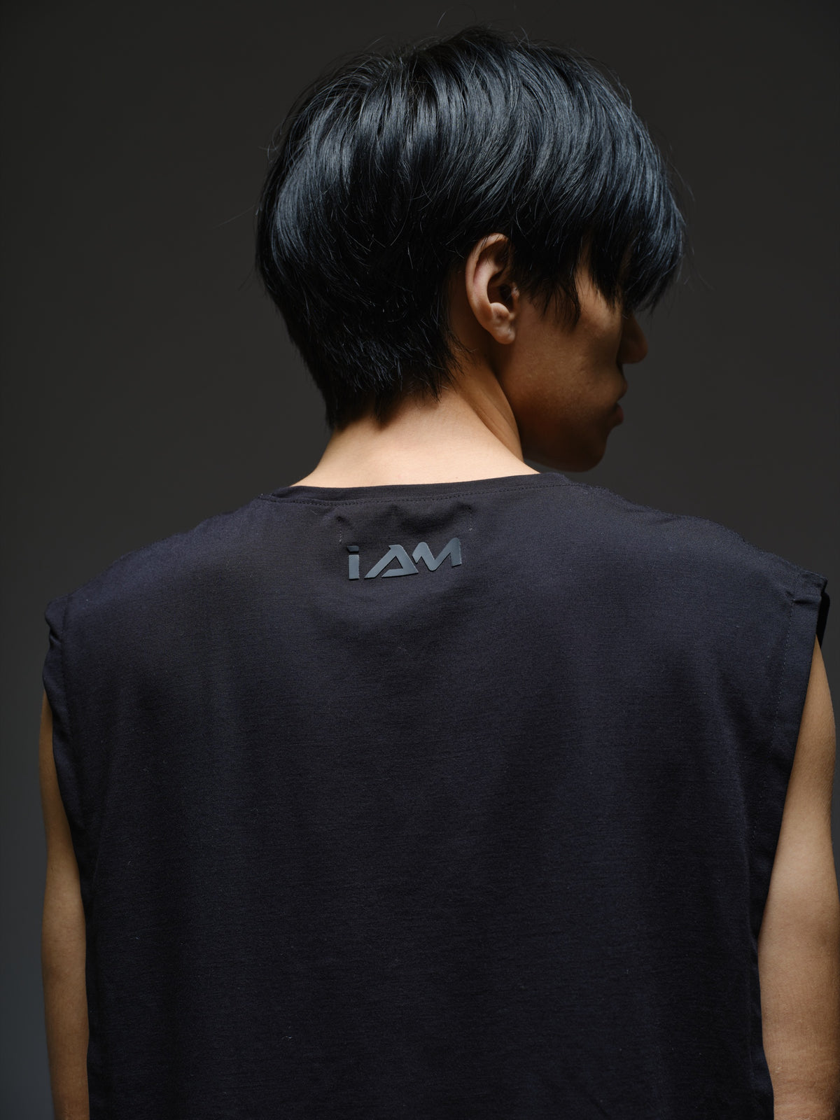 Black sleeveless tee with diagonal panels and leather shoulder patches, paired with black denim track pants with thigh pouch pockets and gathered ankle hems