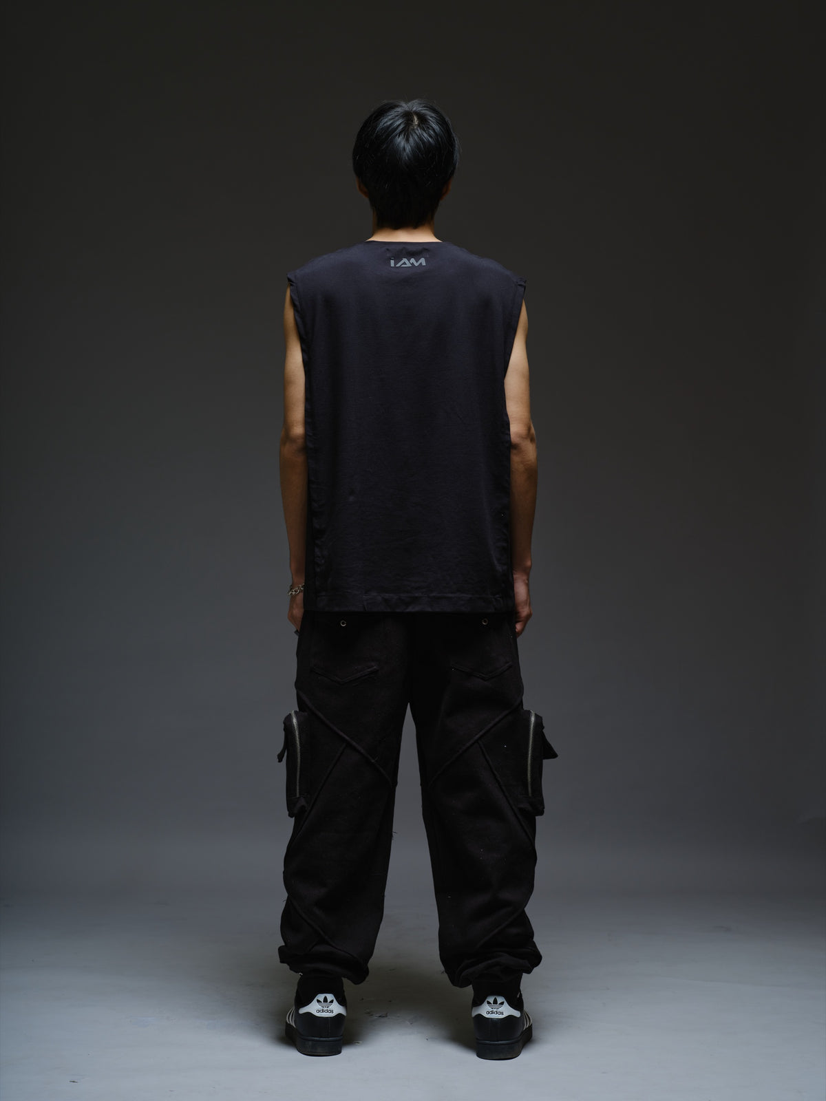 Black sleeveless tee with diagonal panels and leather shoulder patches, paired with black denim track pants with thigh pouch pockets and gathered ankle hems
