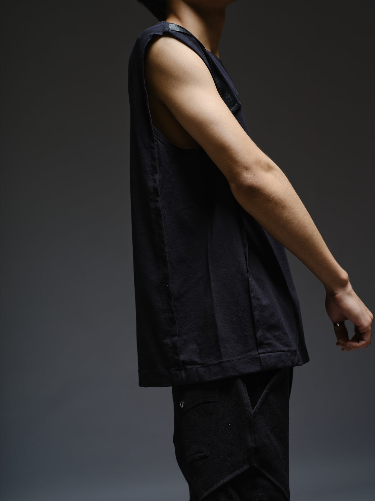 Black sleeveless tee with diagonal panels and leather shoulder patches, paired with black denim track pants with thigh pouch pockets and gathered ankle hems