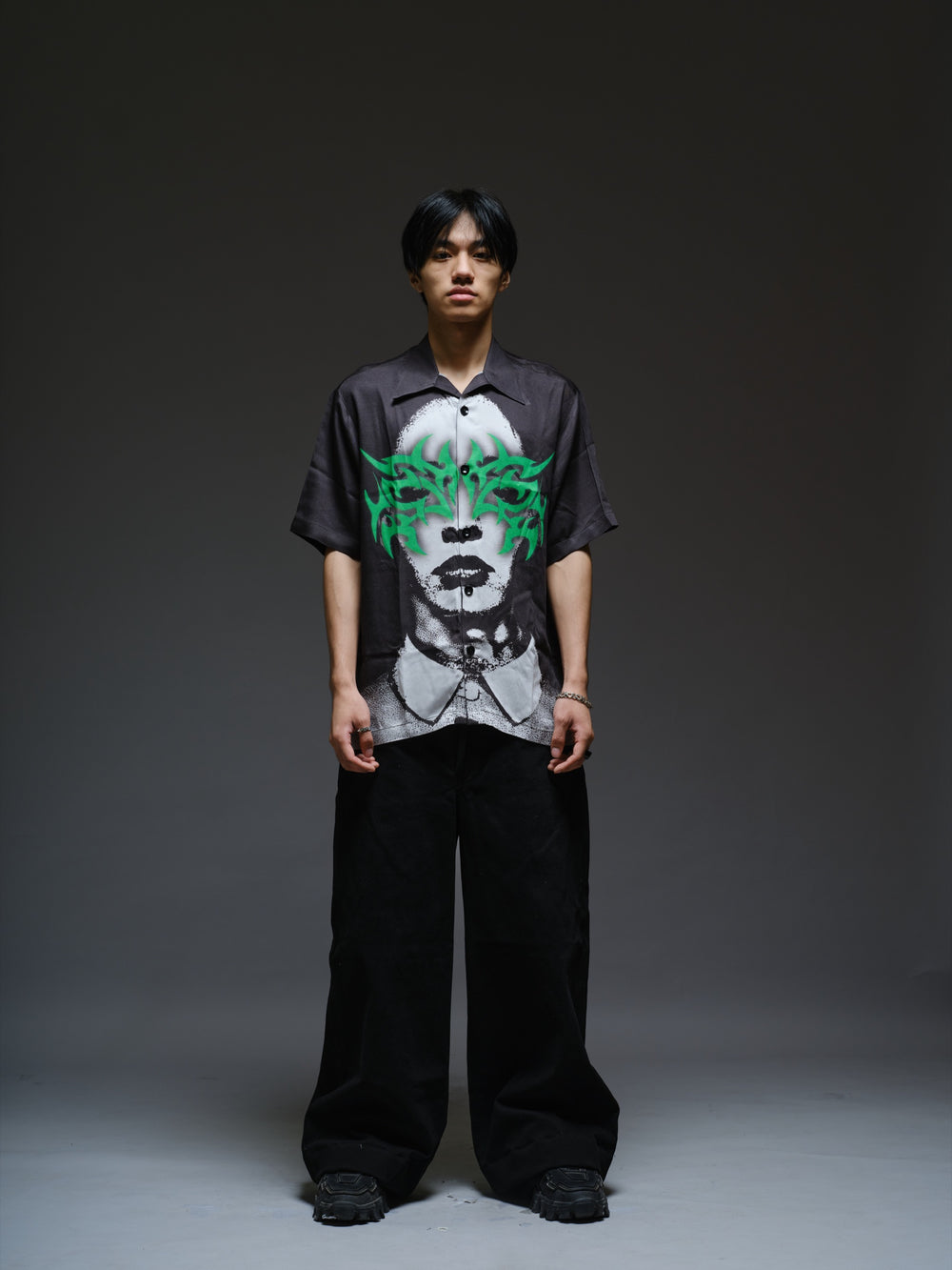 Black oversized short-sleeve shirt with a large monochrome face graphic and an angular green mask across the eyes